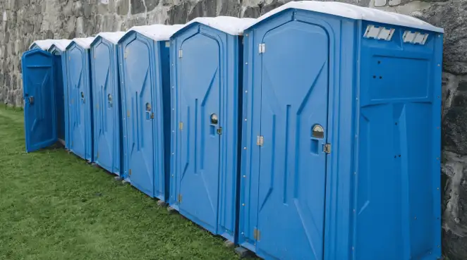 Row of blue portable toilets lined up on grass against a stone wall for event sanitation in Norfolk, VA