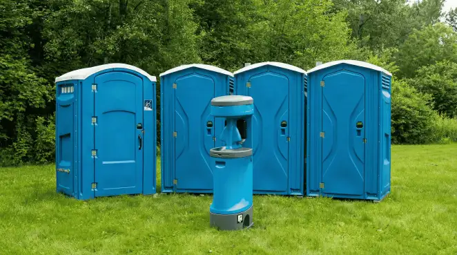 Four blue portable toilets and a matching hand washing station on grass near trees, a common sight at local outdoor events in Norfolk, VA