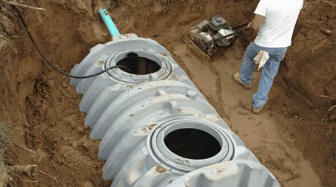 Septic tank installation showing a technician compacting soil around a new poly septic tank in an excavation pit in Norfolk, VA
